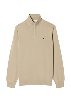 Pull beige à col demi-zip, poignets et ourlet côtelés, avec un petit logo vert sur la poitrine. Tissu tricoté lisse.