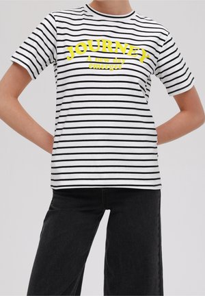 Koszulka w paski w kolorze białym i czarnym, z żółtym napisem. Krótkie rękawy, okrągły dekolt, jednolity kolor u dołu. Materiał to gładka bawełna.