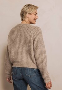 Beiger, gestrickter Pullover mit strukturiertem Rippmuster, rundem Halsausschnitt und leicht gekürztem Schnitt, kombiniert mit blauen Denim-Jeans.