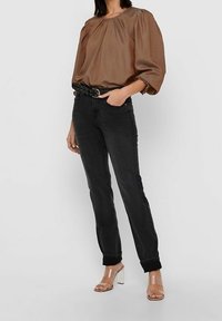 Brązowa bluzka z plisami i bufiastymi rękawami, połączona z czarnymi dżinsami i skórzanym paskiem z ćwiekami. Przezroczyste sandały na obcasie dopełniają look.