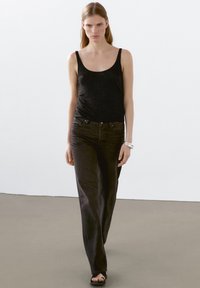 Svart ärmlös linne topp kombinerad med mörka jeans. Klädseln har en figurnära design med en slät yta och minimal detaljering. Sandaler fulländar looken.