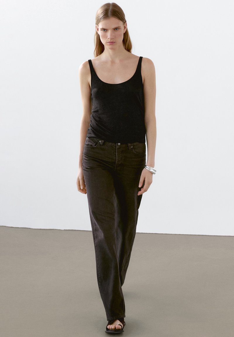 Svart ärmlös linne topp kombinerad med mörka jeans. Klädseln har en figurnära design med en slät yta och minimal detaljering. Sandaler fulländar looken.