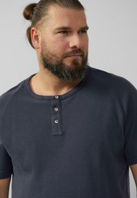 Granatowa koszulka henley z krótkim rękawem, wykonana z teksturowanej tkaniny, z guzikowym zapięciem z drewnianymi guzikami oraz okrągłym dekoltem.