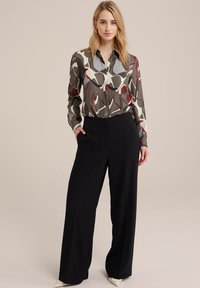 Bluză cu mânecă lungă într-un model abstract colorat, cu nuanțe de gri, roșu și crem; asortată cu pantaloni largi negri cu talie înaltă.