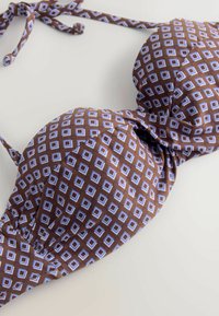Haut de bikini marron avec bonnets rembourrés et motif losanges bleu et blanc, comprenant des bretelles réglables à nouer sur fond blanc.