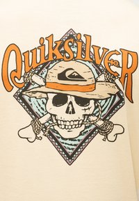 Skalle som bærer en hatt med korslagte bein bak, innrammet av et mønstret diamantformet design og fet oransje "Quiksilver"-tekst.