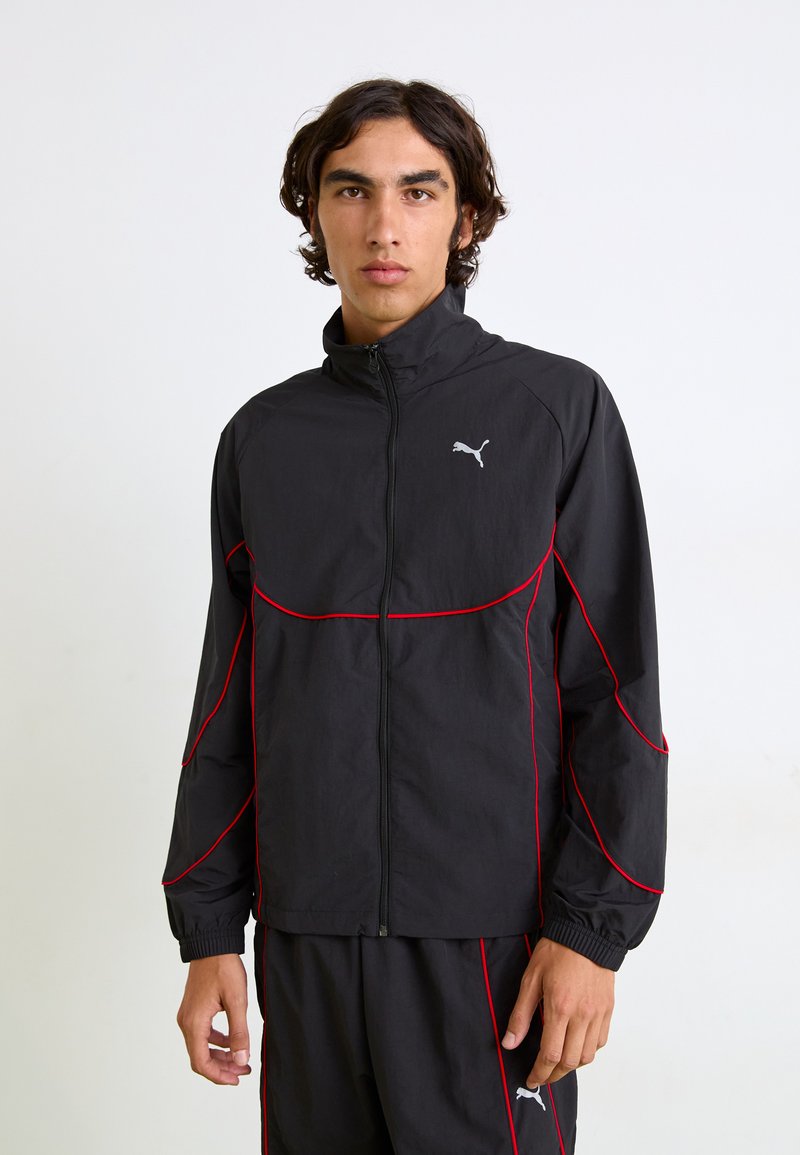 Svart zip-up jakke med røde detaljer og Puma-logo. Har høy krage og elastiske mansjetter, laget av lett, teksturert stoff.