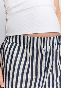 Pantaloni a righe blu navy e crema realizzati in tessuto leggero con vita elasticizzata, caratterizzati da righe verticali e texture morbida.