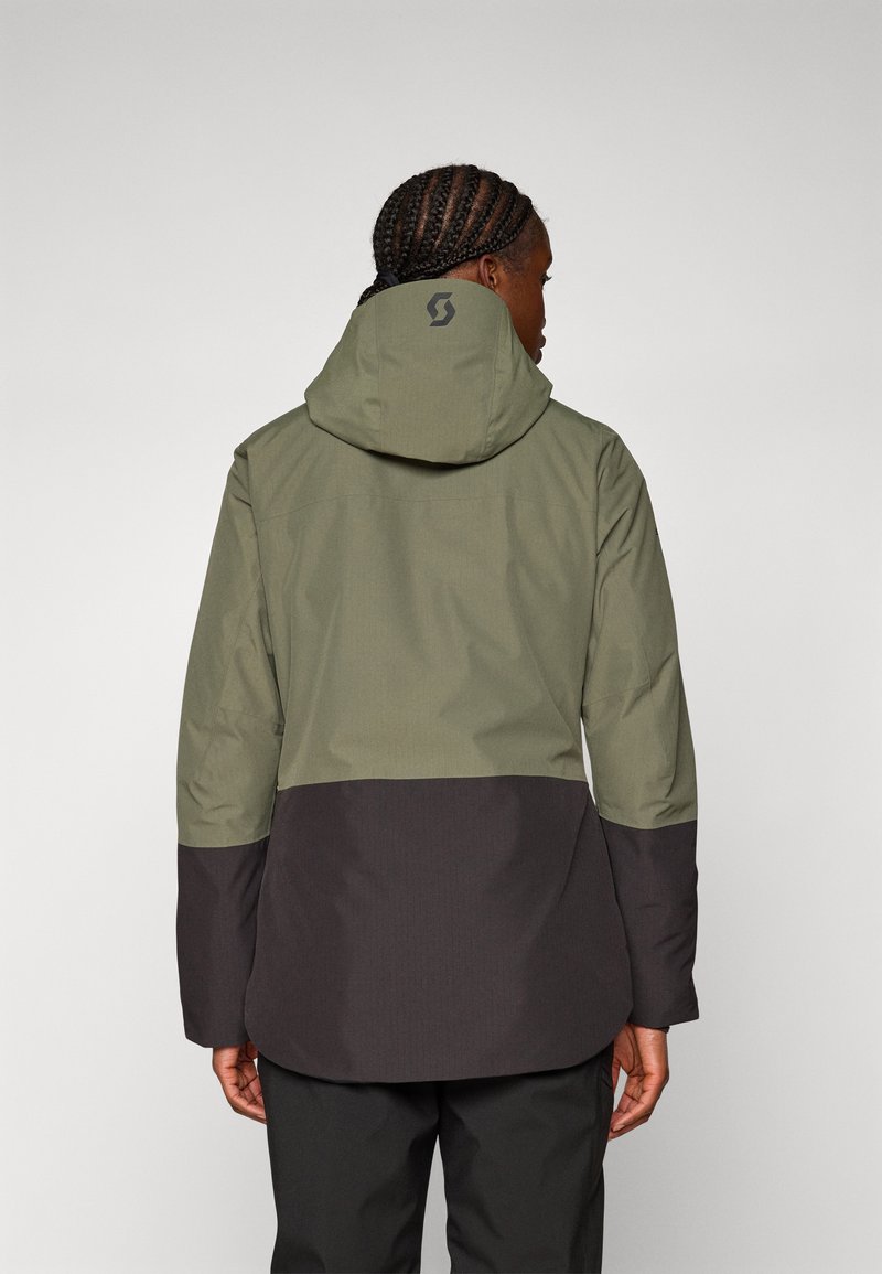 Olivegrüne und dunkelbraune wasserdichte Jacke mit Kapuze, die ein Logo auf dem Rücken, lange Ärmel und eine lässige Passform hat.