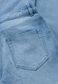 Tissu en denim bleu clair présentant une poche arrière avec une couture visible et une texture lisse. Le design est classique avec un éclat subtil.