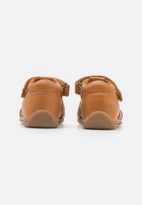 Braune Lederschuhe mit runder Form, Klettverschlüssen und strukturierter Oberfläche. Weiche Sohle mit leichter Wölbung und minimalistischem Design.
