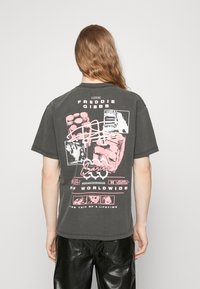 Grafický tričko z tmavě šedé bavlny s krátkými rukávy. Na zadní straně obsahuje růžový text a obrázky, včetně "Freddie Gibbs" a loga.