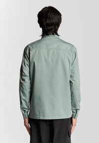Lichtgroene, lichtgewicht jas met lange mouwen, een kraag en een rechte zoom. Glad textiel, geen zichtbare patronen of accenten.