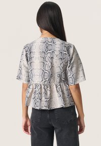 Haut à motif peau de serpent en beige et noir, avec des manches courtes et un ourlet peplum, fabriqué en tissu léger et texturé.