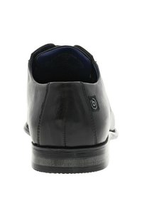 Chaussure en cuir noir avec une texture lisse et un bout arrondi. Présente un petit talon et une petite étiquette de logo noire à l'arrière.