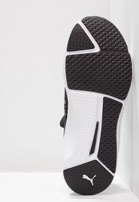 Svart och vit träningsskosula med en texturerad, mönstrad svart gummiyta och en slät vit mellansula; har detaljer med varumärkeslogotyp.