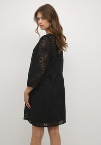 Schwarzes Spitzenkleid mit Blumenmustern, 3/4-Ärmeln, tailliertem Schnitt und knielangem Saum. Durchsichtige Textur hebt das filigrane Design hervor.