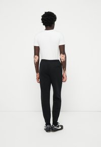 Sorte sweatpants med elastisk talje og tætsiddende manchetter, parret med en almindelig hvid t-shirt, set bagfra, iført sorte sneakers.