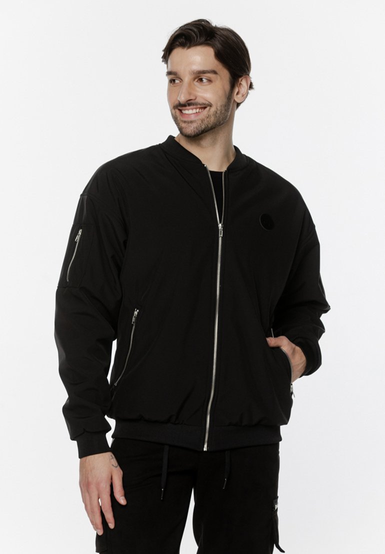 Czarna bomberka z zamkiem z przodu, ściągaczami przy mankietach oraz dwoma zasuwanymi kieszeniami po bokach. Posiada mały, okrągły emblemat na piersi.