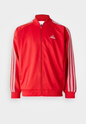 Sarkans sporta jaka ar augstu apkakli, priekšējo rāvējslēdzēju, baltām trīs svītrām uz piedurknēm un ribota apakšmalu un piedurknēm. Logo uz krūšu.