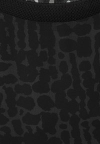 Zwarte stof met een gestructureerd, abstract patroon met verschillende vormen. Het materiaal heeft een lichte glans en is omzoomd met een gestructureerde zwarte band.