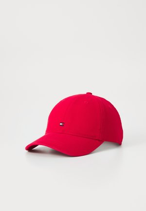 Casquette de baseball rouge avec une visière courbée et un petit logo rectangulaire à l’avant, posée sur une surface blanche.