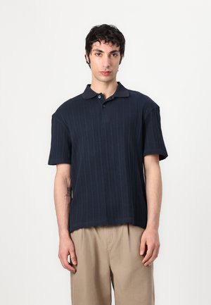 Navy blue polo shirt with a ribbed texture, short sleeves, and a classic collar, featuring two buttons on the placket.