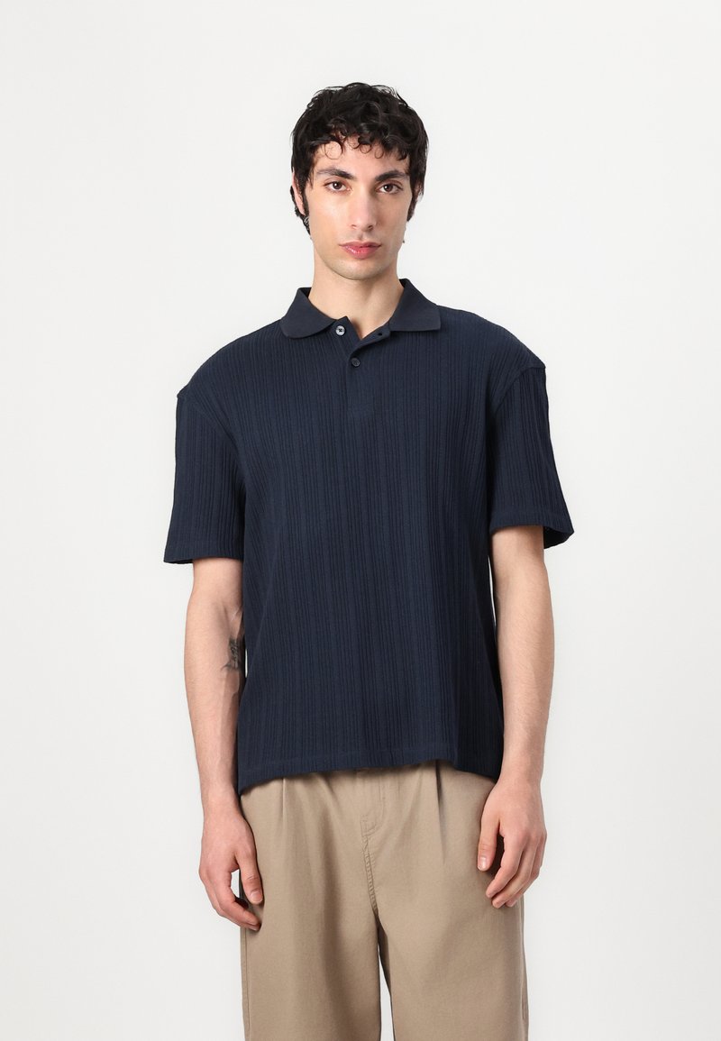 Navy blue polo shirt with a ribbed texture, short sleeves, and a classic collar, featuring two buttons on the placket.