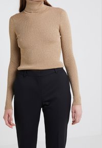 Beige ribbad polokrage tröja gjord av ett strukturerat tyg, kombinerad med svarta skräddarsydda byxor. Toppens design har långa ärmar och en åtsittande passform.