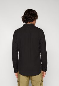 Μαύρο πουκάμισο με κουμπιά και μυτερό γιακά, διαθέτει μακριά μανίκια, ίσια γραμμή και ετικέτα logo στην πλάτη. Φτιαγμένο από υφασμάτινη υφή.