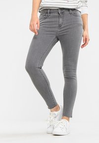 Jeans ajustados de denim gris con cintura alta, con un dobladillo deshilachado y diseño clásico de cinco bolsillos, combinados con zapatillas blancas.