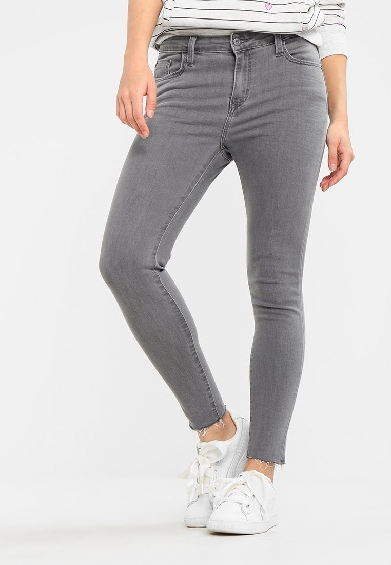 Jeans ajustados de denim gris con cintura alta, con un dobladillo deshilachado y diseño clásico de cinco bolsillos, combinados con zapatillas blancas.