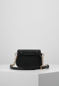 Sort læder skuldertaske med guldkæde-detaljer. Har en rundet form, flad top og en simpel lås. Justerbar rem medfølger.