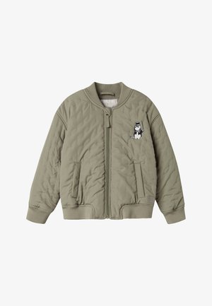 Χακί πράσινο καπιτονέ μπουφάν μπόμερ με ριμπ γιακά, μανσέτες, ζώνη στη μέση, εμπρόσθιο φερμουάρ, τσέπες και ένα μικρό ασπρόμαυρο καρτούν χαρακτήρα στο στήθος.