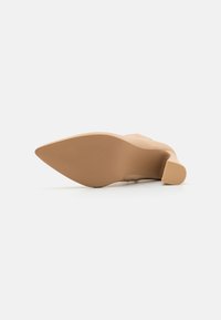 Zapato de tacón desnudo con punta afilada y suela texturizada. El tacón es de altura moderada con un diseño robusto en bloque.
