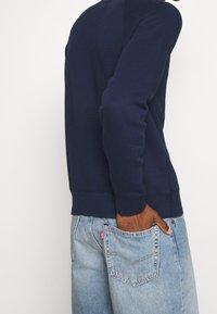 Námořnická modrá mikina s kulatým výstřihem a dlouhými rukávy, s vroubkovanými manžetami a lemem, v kombinaci s světle modrými džíny. Měkká tkanina, volný střih.