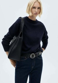 Pulover bleumarin cu guler rotund, asortat cu blugi negri din denim, o curea neagră cu cataramă din argint și o geantă de umăr neagră.