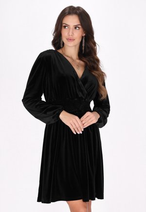 Musta samettipeiteline dress, jossa on pitkät hihat ja kerroksellinen vyötärö. Ominaisuuksiin kuuluu syvä V-muotoinen kaula-aukko ja virtaava hame, joka luo pehmeän siluetin.