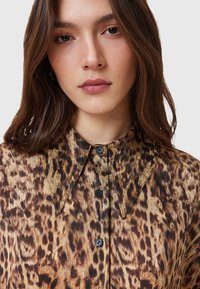 Camicia con stampa leopardata dal texture morbido, colletto a punta, bottoni neri e una palette di colori marrone e tan.