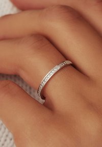 Bague en argent avec un anneau lisse et une rangée de petites pierres étincelantes sur un côté, reposant sur une main légèrement texturée.