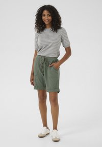 Chemise à manches courtes rayée grise et blanche, associée à un short vert avec cordon de serrage. Le short possède deux poches latérales et des ourlets retroussés. Baskets blanches.