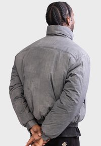 Grå polstret jakke med høj krave, der har en glat tekstur og ribbede manchetter. Den har en afslappet pasform og let afrundede skuldre.