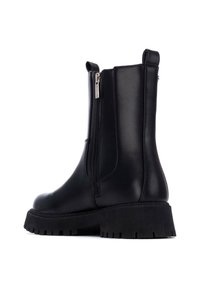 Botas hasta el tobillo de cuero vegano negro con cremallera lateral, suela gruesa y suela de goma texturizada para mayor agarre. Diseño de punta redondeada.