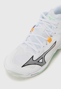 White athletic shoe features a textured mesh upper, black wave design, orange accents, and a green-tinged sole with "Mizuno Enerzy" branding.