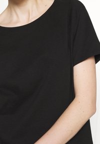 Černé bavlněné tričko s kulatým výstřihem a krátkými rukávy, s hladkou texturou. Detailní záběr zdůrazňující ležérní střih.