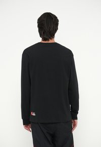 Μαύρο μακρυμάνικο t-shirt από μαλακό βαμβάκι με στρογγυλή λαιμόκοψη, ραμμένα μανίκια και μια μικρή ετικέτα του σήματος κοντά στο στρίφω.