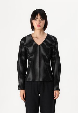 Haut noir à manches longues avec un décolleté en V et des rayures verticales blanches, présentant un design ajusté et une texture de tissu lisse. Associé à un pantalon noir.