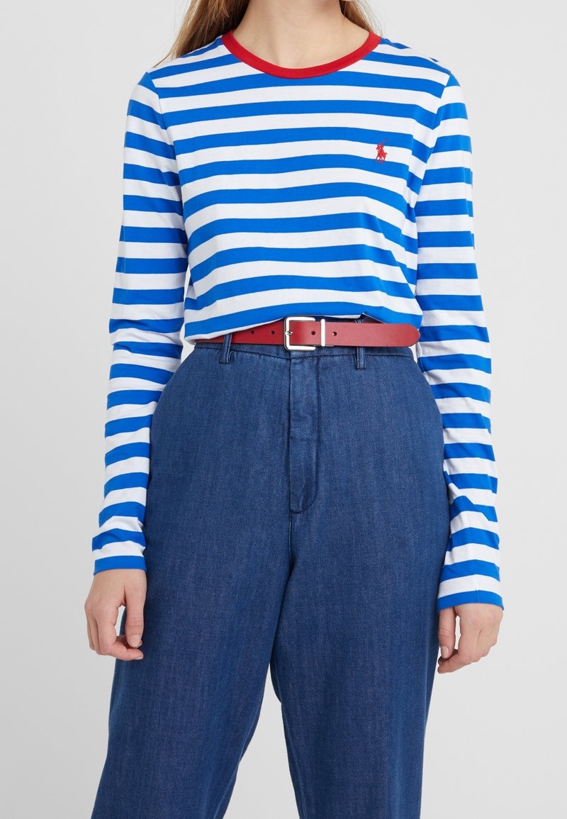 Långärmad skjorta med blå och vita horisontella ränder, röd rundhalsad krage och en liten logotyp. Matchas med högmidjade blå denimbyxor och röd bälte.