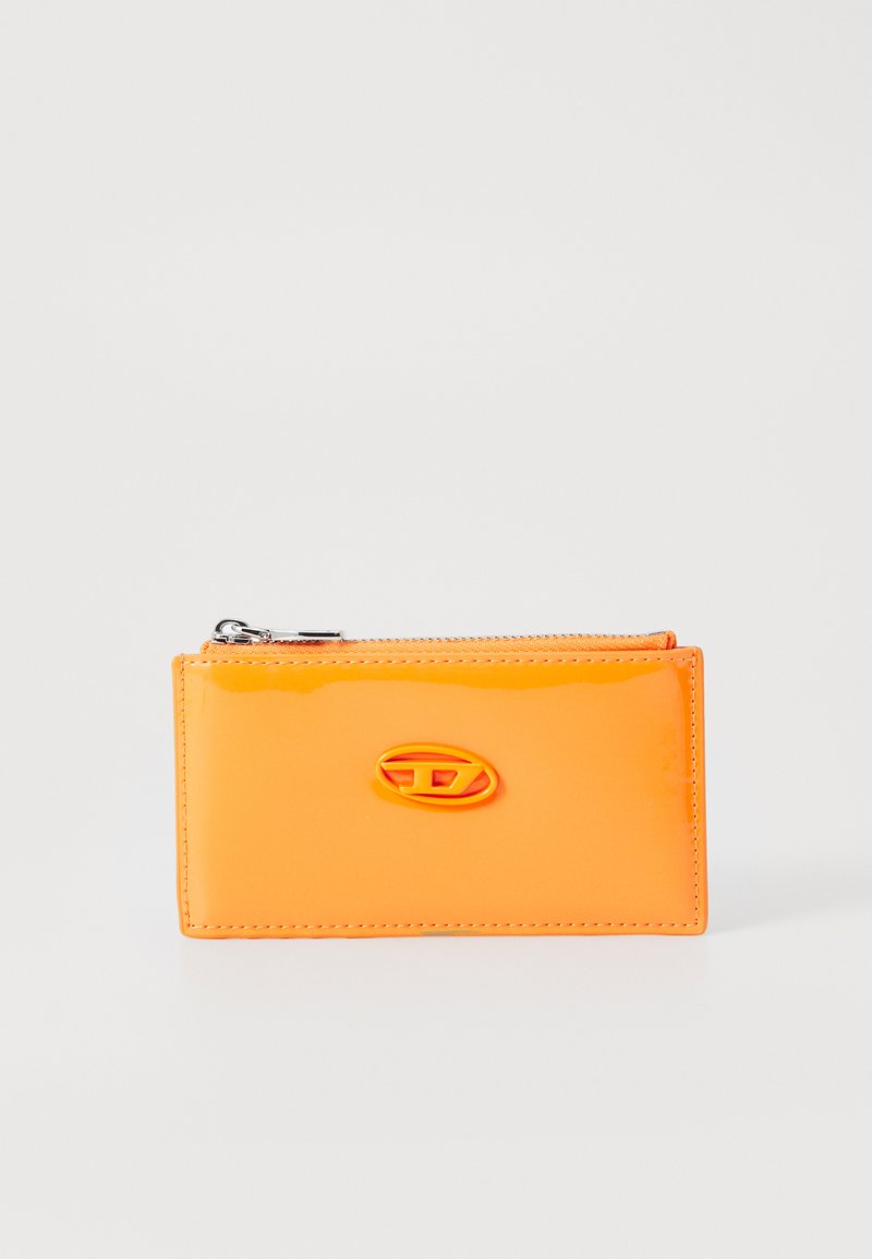 Λαμπερό πορτοφόλι από πατεντωμένο δέρμα σε έντονο πορτοκαλί χρώμα, με κλείσιμο φερμουάρ και ανάγλυφο λογότυπο. Μινιμαλιστικός ορθογώνιος σχεδιασμός, λεία υφή και καθαρές γραμμές.