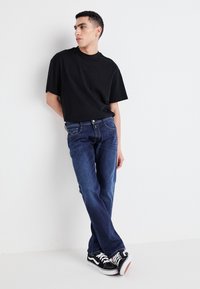 Svart kortärmad t-shirt, blå denimjeans och svarta Vans-sneakers. Slim fit-jeans med synlig sömnad och lätt blekning.